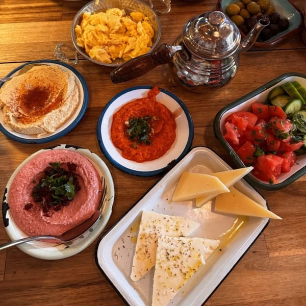 Turkish breakfast spread with various dips, cheeses, scrambled eggs, and a silver teapot on a wooden table.