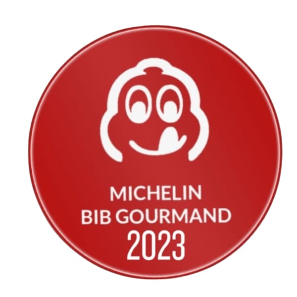 Red Michelin Bib Gourmand 2023 award logo with a smiling, tongue-licking chef icon.