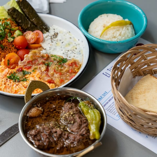 A Turkish breakfast spread with various dishes, including rice, meat stew, and a salad with dolmas.