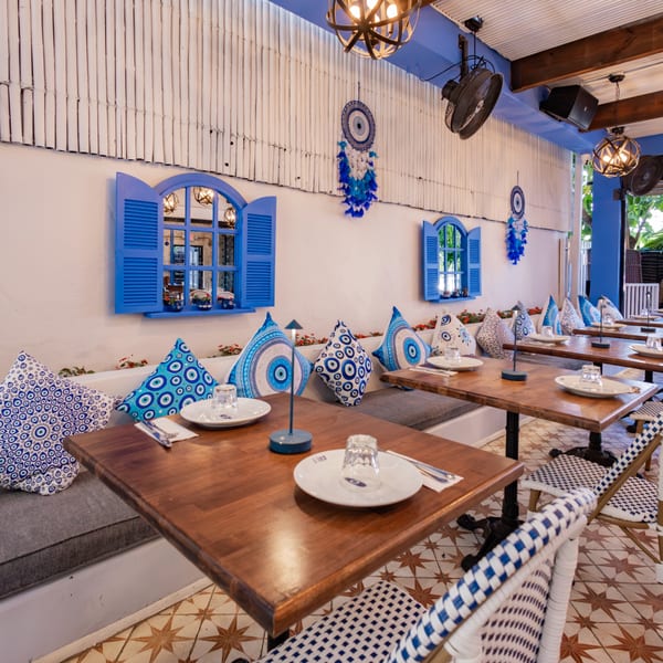 A vibrant restaurant interior with blue and white decor, wooden tables, and patterned cushions.