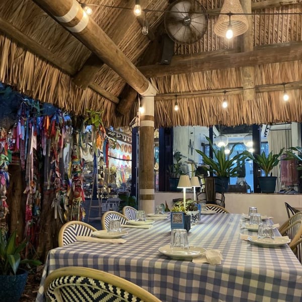 A long dining table with a blue and white checkered tablecloth in a rustic, open-air restaurant.