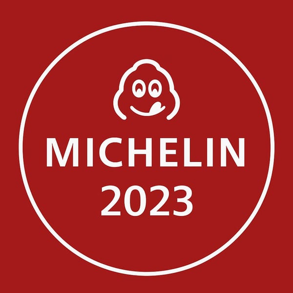 Red circular Michelin Guide 2023 logo with a white smiling chef icon.