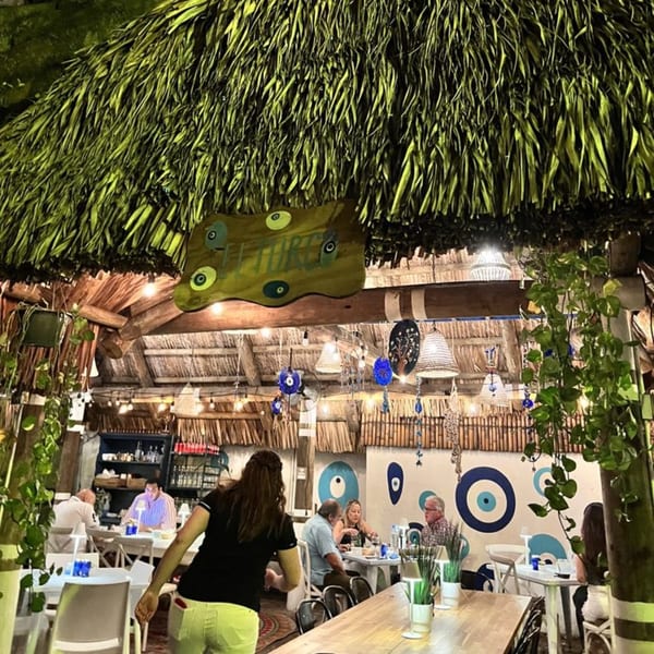 Diners seated at tables under a thatched roof, with Turkish evil eye decor on the walls.