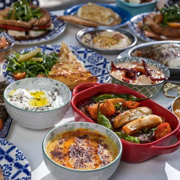 A table laden with various Turkish dishes, including yogurt, hummus, pastries, and a meat dish.